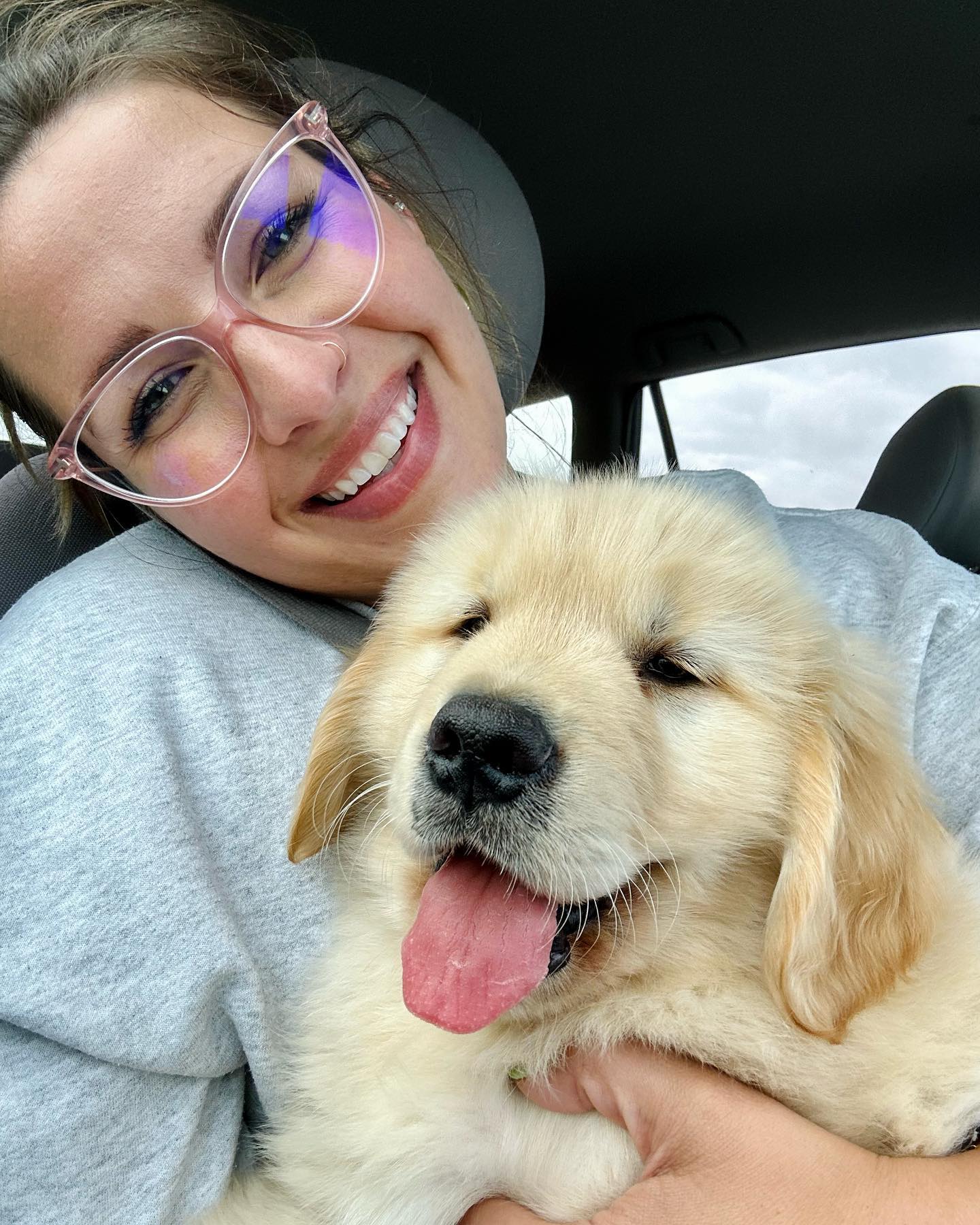Woman with a big smile holding a golden retriever puppy.