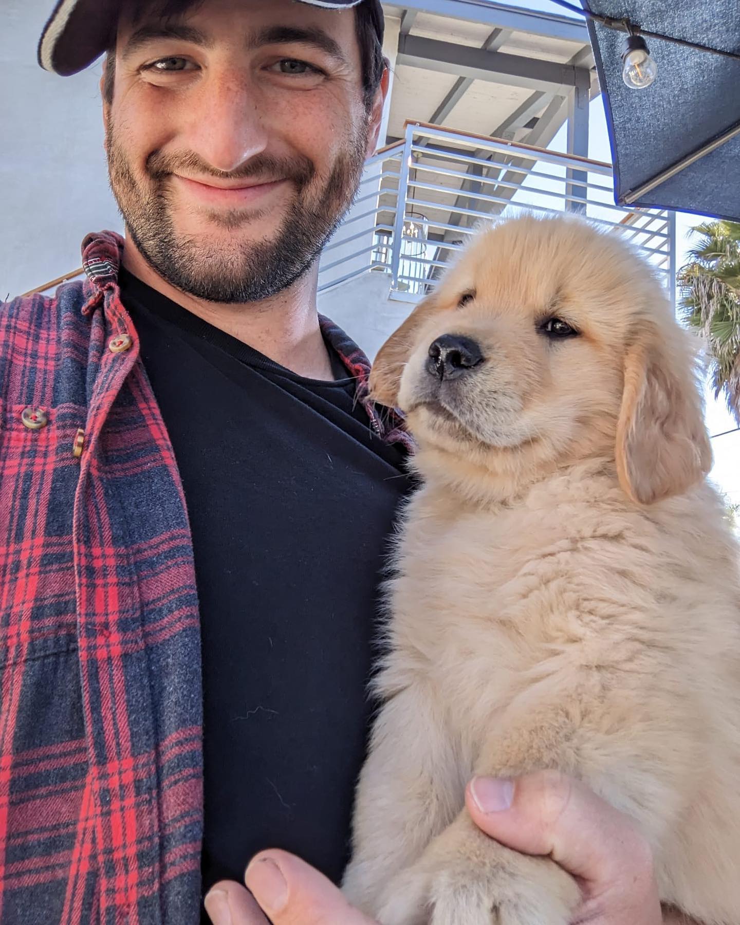 Man smiling while holding a golden retriever puppy.